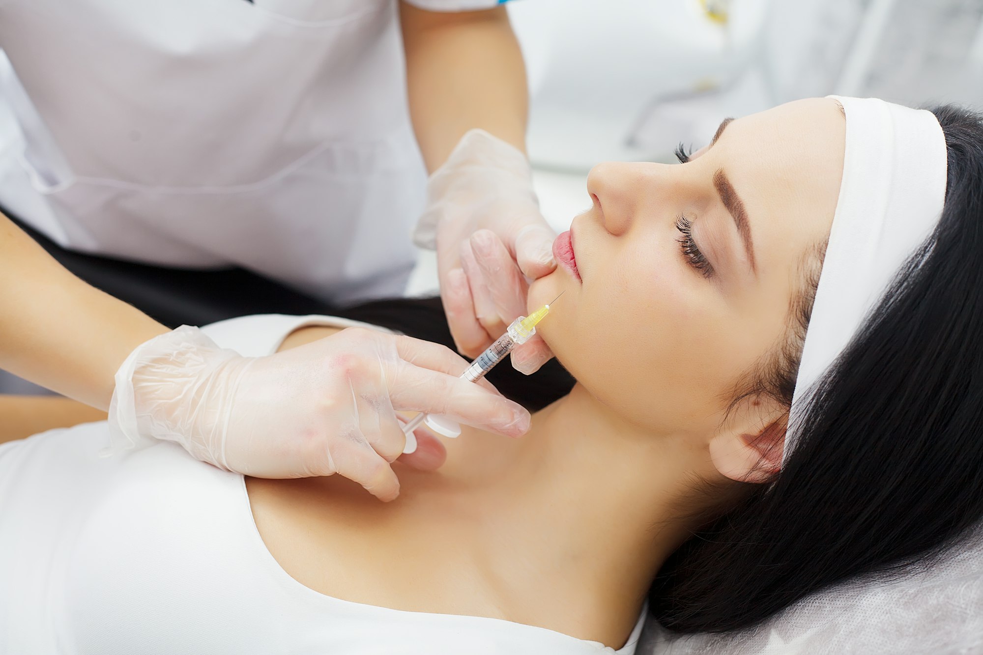 Woman receiving a botox injection in the lips zone lying in bathrobe on the medical couch